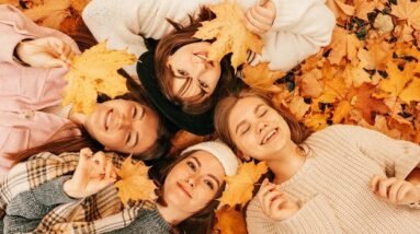 Smiling women lying on the ground in fall leaves.