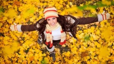 A woman standing in fall leaves with a smile.