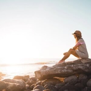 A woman sitting on a rock by the ocean and watching the view.