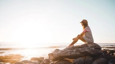 A woman sitting on a rock by the ocean and watching the view.