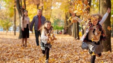 Children running and throwing autumn leaves while their parents watch them smiling.