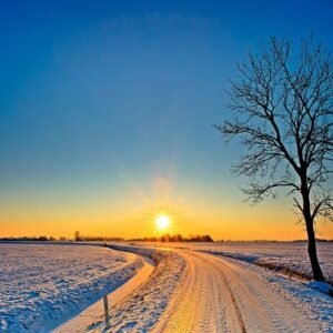 A small road with a beautiful sunrise over a snow covered and open landscape.