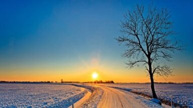 A small road with a beautiful sunrise over a snow covered and open landscape.