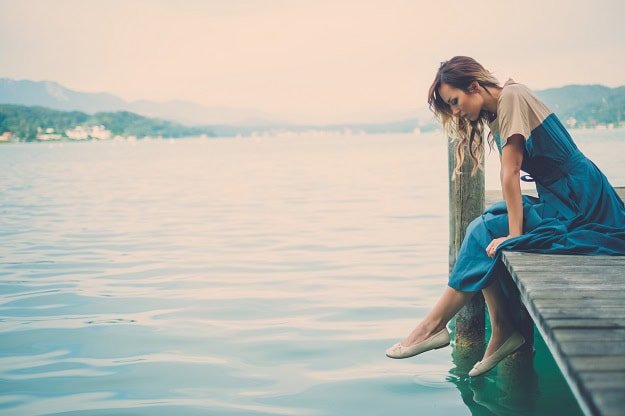 A woman sitting on a pier with mountain lake view.