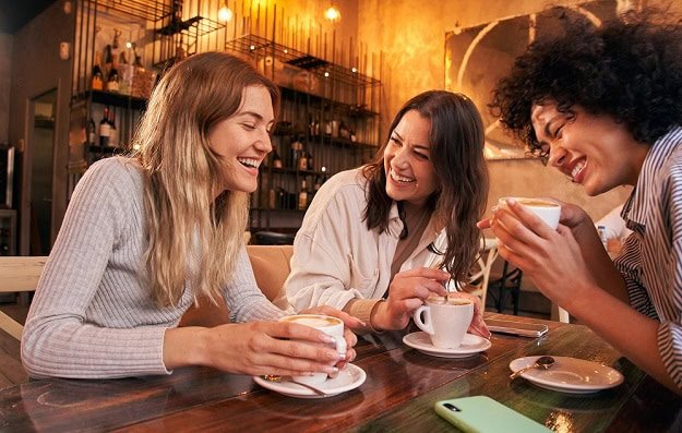 Three laughing women having a cup of coffee.