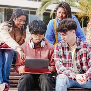 Students looking at a laptop while sitting on a bench outside school.