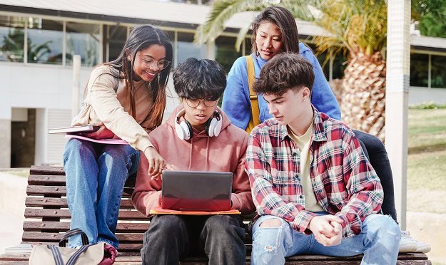 Students looking at a laptop while sitting on a bench outside school.