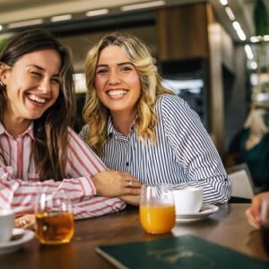 Two happy women smiling into the camera while at a coffee shop.