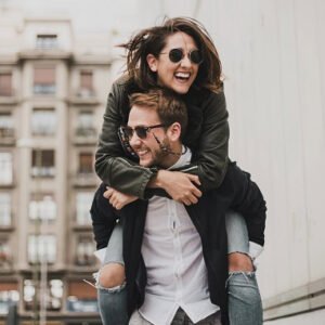 A happy couple outside with the man giving the woman a piggyback ride.