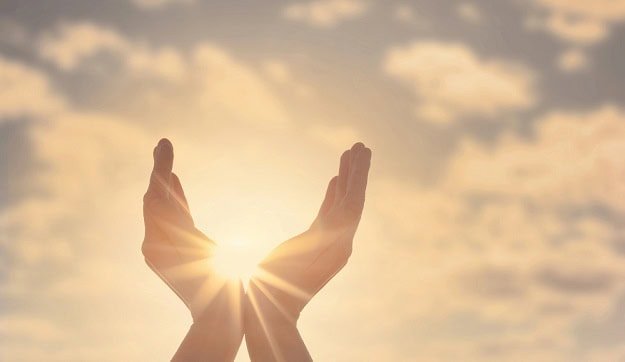 Two hands reaching towards the sky with the sun in the background.