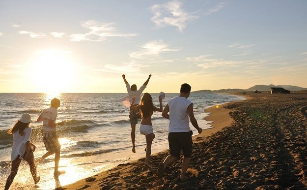 Friends running on the beach during a summer sunset.