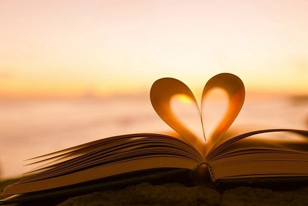 A heart made of two pages in an open book with a sunrise on the horizon.