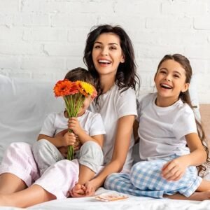 A happy mother with her two smiling children in bed and a bouquet of flowers.