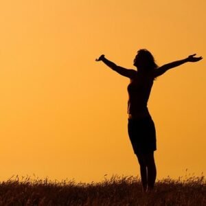 A woman at sunrise outside stretching her arms towards the sky.,