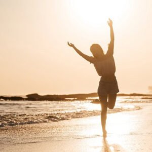 A happy woman dancing on the beach by the waters edge.