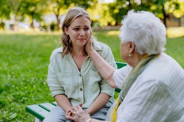 An older woman comforting a sad young woman while they sit on a park bench.