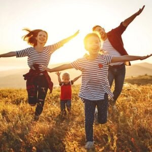A happy family running towards the camera in a field of grass with their arms stretched out imitating airplanes.