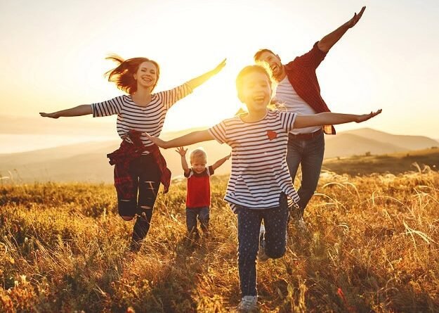 A happy family running towards the camera in a field of grass with their arms stretched out imitating airplanes.